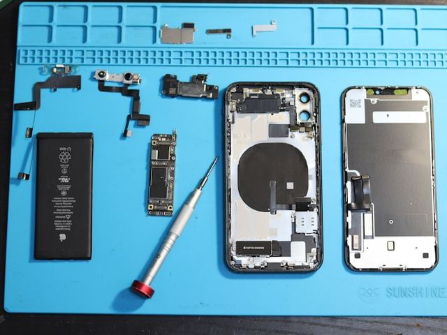Losgekoppelde telefoonbatterij naast onderdelen op een blauwe reparatiemat