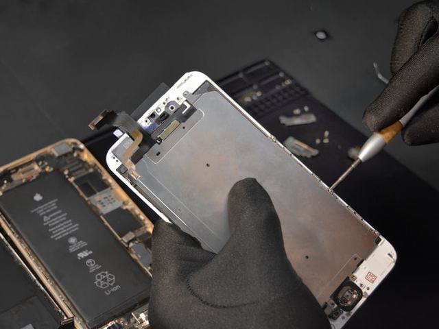 Technicus tilt een gebarsten telefoonscherm van de behuizing
